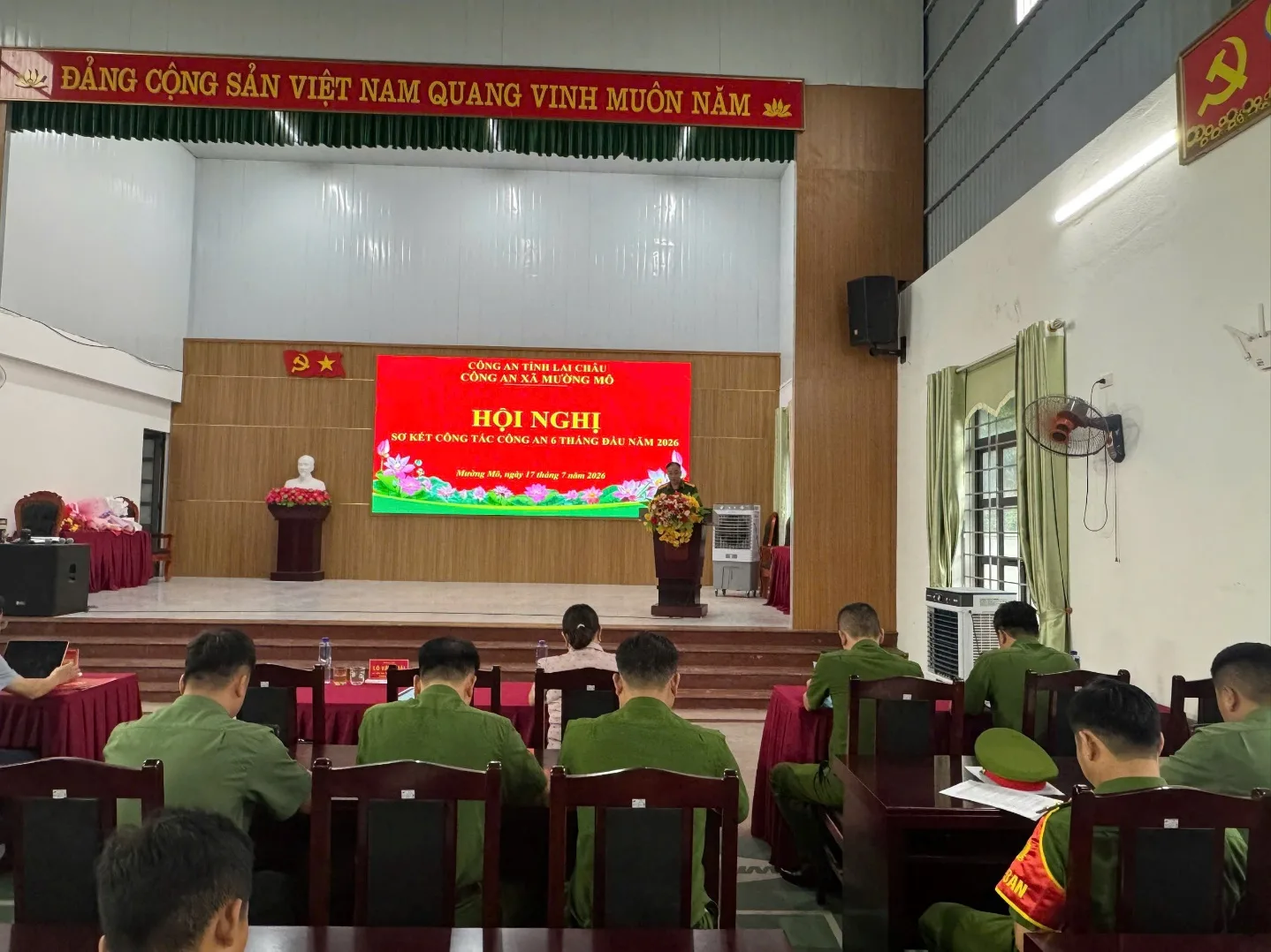 A group of people in green uniforms sitting in chairs in front of a stageDescription automatically generated